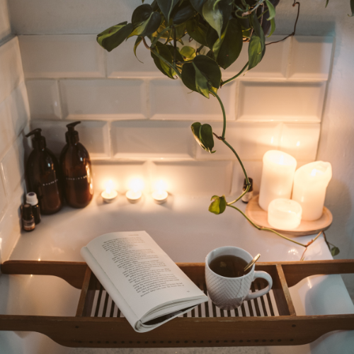 cup of tea and book with candles on a shelf over a bath.