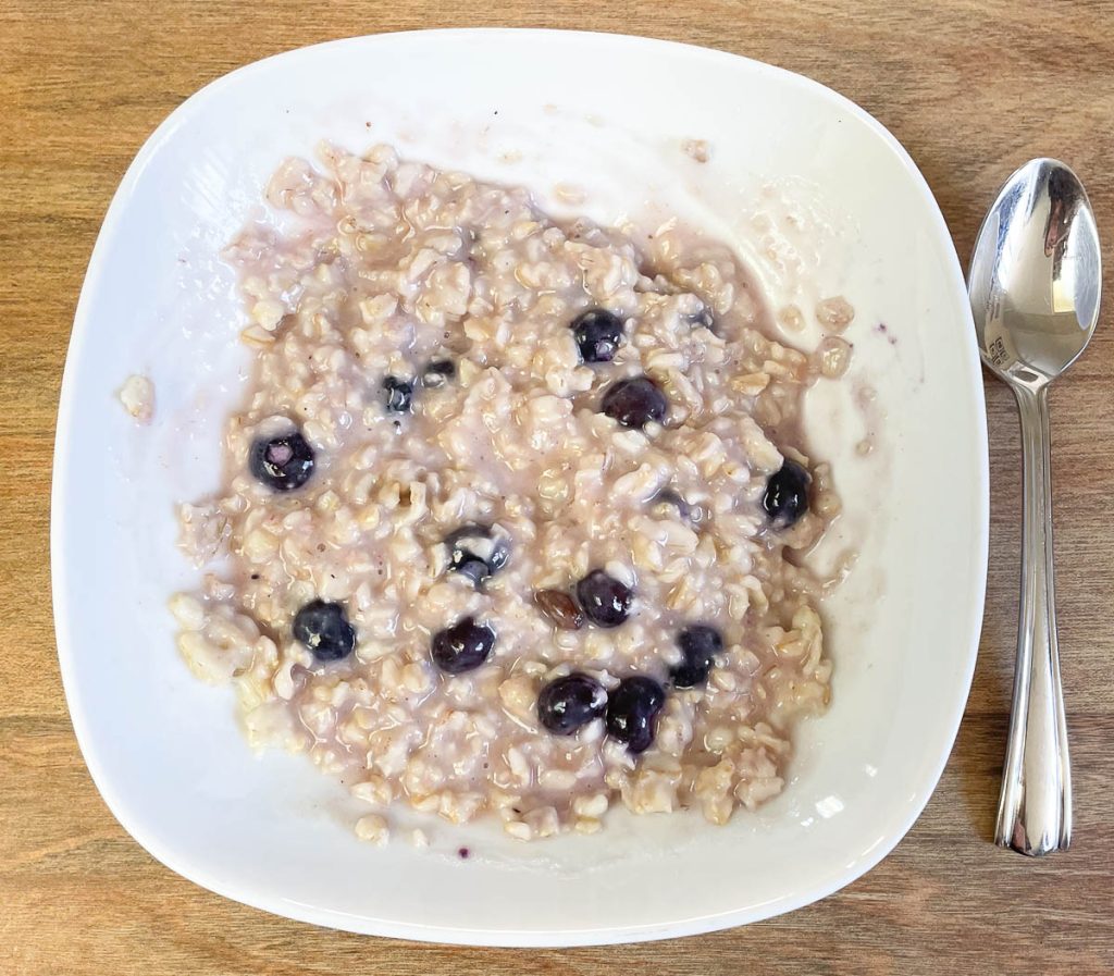 A bowl of oatmeal with blueberries and a spoon next to it.