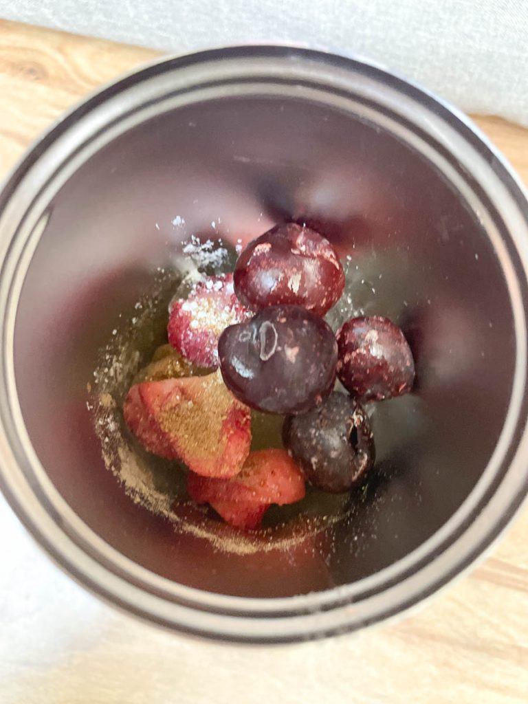 A cup with ice, cherries, strawberries, and powdered ingredients in it. A top angle looking down into it.