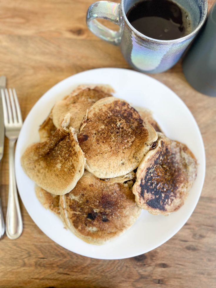 Pancakes on a plate with a fork and a cup of coffee