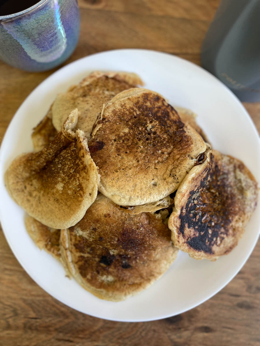 Pancakes on a plate next to a cup of coffee